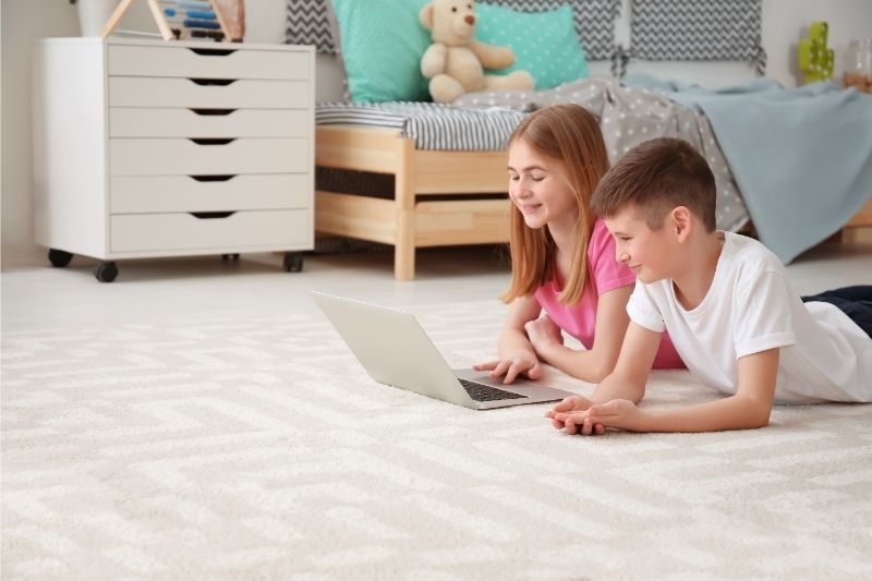 two children using a laptop while lying on the floor